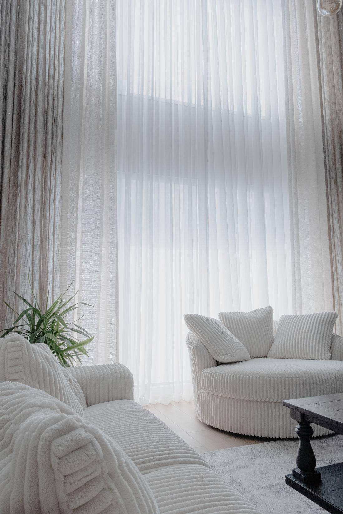 Soft white curtains, pale walls and cream upholstered furniture in a tonal living room