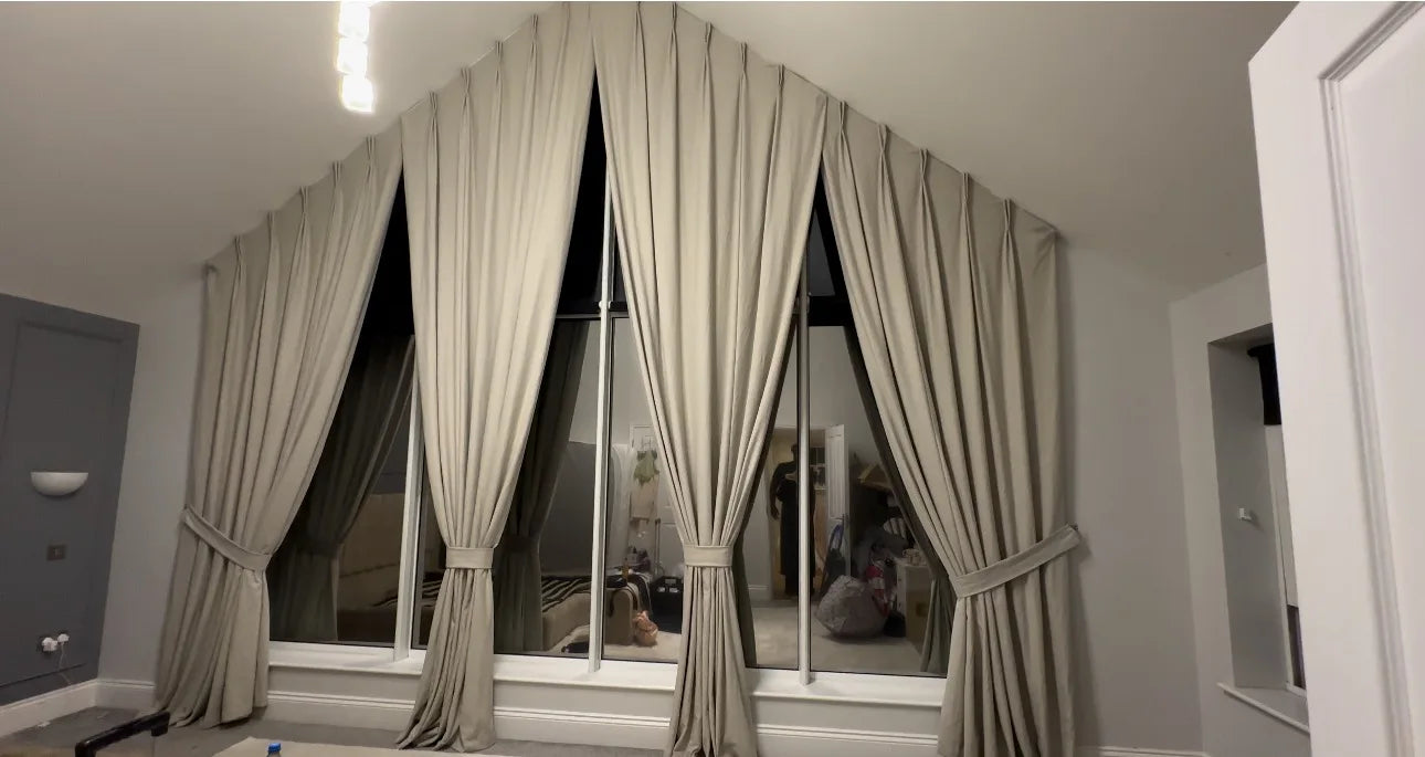 Pale bespoke curtains following an apex roofline, gathered into matching tiebacks